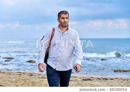 Serious confident successful mature man walking along the beach. Serious confident successful mature man walking along the beach. 89190059