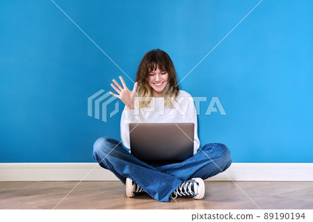 Beautiful teenage female sitting on the floor with laptop on blue background Beautiful teenage female sitting on the floor with laptop on blue background 89190194