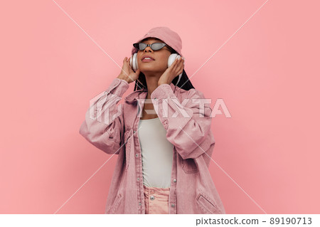 Monochrome portrait of young attractive happy woman in casual style outfit listening to music isolated on pink background. Concept of beauty, art, fashion, youth, style 89190713