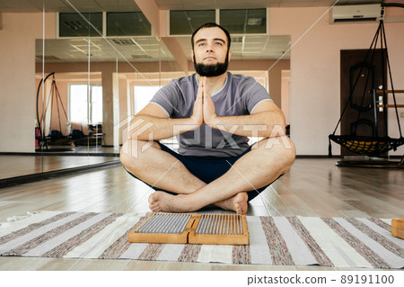Man exercising yoga meditating sitting hands joined on the floor near sadhu board Man exercising yoga meditating sitting hands joined on the floor near sadhu board 89191100