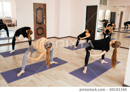 Girls in sportswear working out in fitness hall. Young fit women doing yoga pose exercise on mats in gym 89191386