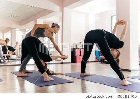 Yoga teacher and beginner in class, making asana exercises. Healthy lifestyle in fitness club. Stretching with coach Yoga teacher and beginner in class, making asana exercises. Healthy lifestyle in fitness club. Stretching with coach 89191409