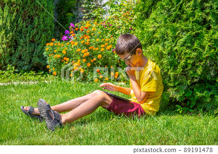 Boy holding tablet PC on green grass lawn Boy holding tablet PC on green grass lawn 89191478