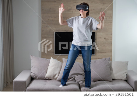Happy young woman playing on VR glasses indoor, Virtual reality concept with young girl having fun with headset goggles, with copy space Happy young woman playing on VR glasses indoor, Virtual reality concept with young girl having fun with headset goggles, with copy space 89191501