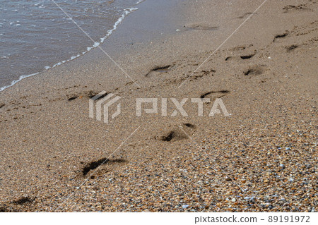 Footprints of a man on the yellow beach sand from walking barefoot by the sea with water  89191972