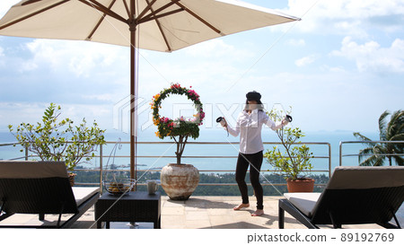 The girl is standing on the terrace of the villa in virtual reality glasses on the sea view background 89192769