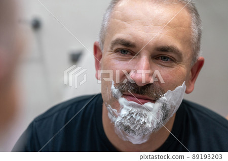 Middle aged handsome man shaving his beard in bathroom Middle aged handsome man shaving his beard in bathroom 89193203