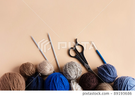 Blue, gray and brown balls of knitting thread with scissors, crochet and knitting needles on a beige background for hobbies. Flat lay 89193686