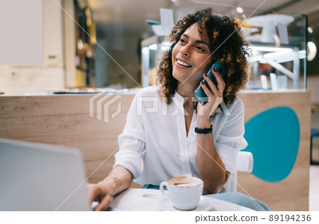 Cheerful female freelancer with netbook talking via cellphone app Cheerful female freelancer with netbook talking via cellphone app 89194236