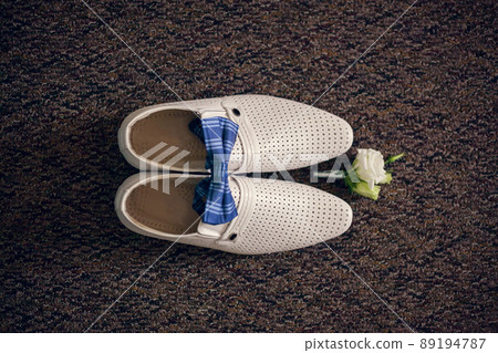 Groom's white shoes, bow tie and boutonniere, top view. Groom's morning, wedding details, preparation for the wedding ceremony Groom's white shoes, bow tie and boutonniere, top view. Groom's morning, wedding details, preparation for the wedding ceremony 89194787