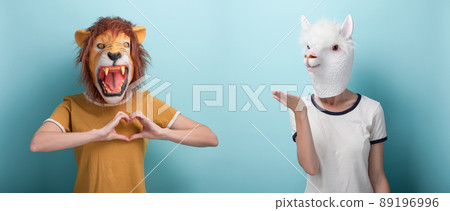 Woman in lion mask shows love hand gesture, and woman in alpaca mask blows and send air kiss Woman in lion mask shows love hand gesture, and woman in alpaca mask blows and send air kiss 89196996