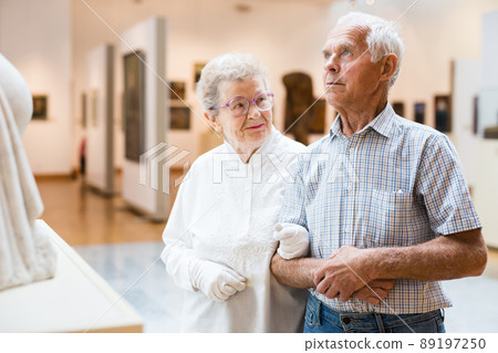 mature European couple examines paintings in an exhibition in hall of art museum 89197250