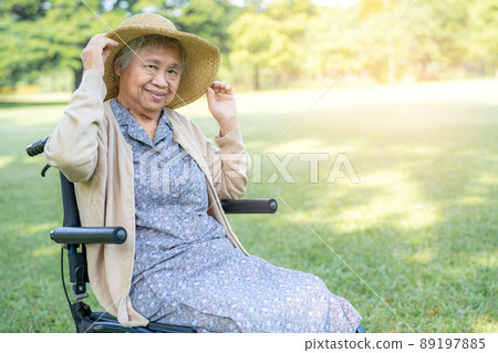 An elderly woman traveler with straw hat sitting on wheelchair in park. 89197885