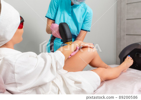 Professional cosmetologist in pink gloves removes hair with laser epilation to the client's female hand. The concept of professional care procedure in a beauty salon Professional cosmetologist in pink gloves removes hair with laser epilation to the client's female hand. The concept of professional care procedure in a beauty salon 89200586