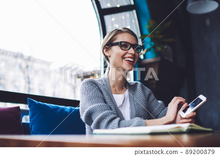 Delighted woman with smartphone resting in cafe 89200879
