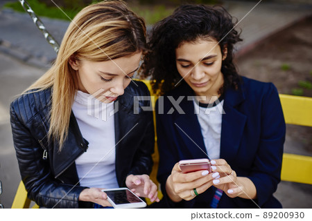 Multiracial ladies sitting on bench while text messaging on mobiles Multiracial ladies sitting on bench while text messaging on mobiles 89200930