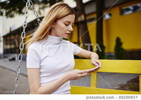 Female sitting on bench with mobile in park 89200937