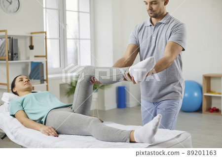Physiotherapist examines patient's leg and exercises with her in rehabilitation center. 89201163