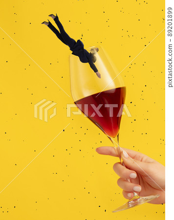Contemporary art collage. Woman in a suit diving into wine glass isolated over yellow background Contemporary art collage. Woman in a suit diving into wine glass isolated over yellow background 89201899