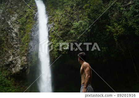 Shirtless Man sitting in front of La fortuna waterfall in Costa Rica Shirtless Man sitting in front of La fortuna waterfall in Costa Rica 89201916