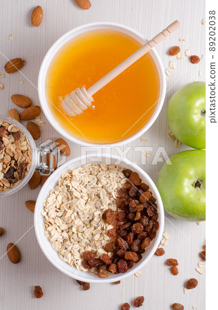 Healthy Breakfast. Oatmeal with raisins in white bowl. Almonds, apple, honey on white table background Healthy Breakfast. Oatmeal with raisins in white bowl. Almonds, apple, honey on white table background 89202038