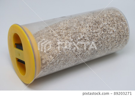 oatmeal in a transparent plastic food jar with a yellow lid on a white background. 89203271