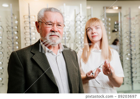 an elderly man with an ophthalmologist chooses glasses in the optics salon. an elderly man with an ophthalmologist chooses glasses in the optics salon. 89203697