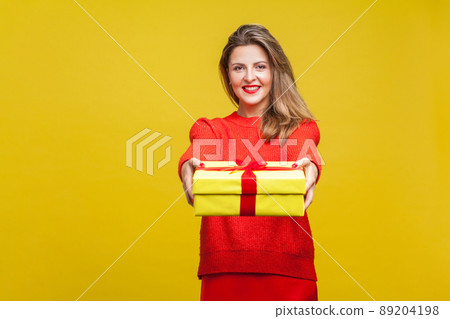 Portrait of happy beautiful blonde woman with red lipstick in bright casual sweater, giving wrapped gift box to camera, christmas present. indoor studio shot isolated on yellow background Portrait of happy beautiful blonde woman with red lipstick in bright casual sweater, giving wrapped gift box to camera, christmas present. indoor studio shot isolated on yellow background 89204198