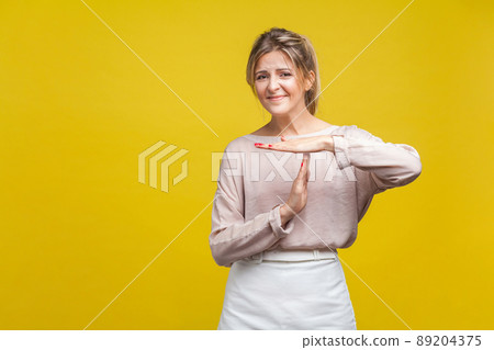 I need more time. Portrait of tired upset young woman with fair hair in casual beige blouse standing showing timeout gesture, looking at camera asking. indoor studio shot isolated on yellow background 89204375