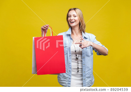 Portrait of cheerful shop customer, happy woman pointing at bags and looking at camera with toothy smile, satisfied with discounts. indoor studio shot isolated on yellow background Portrait of cheerful shop customer, happy woman pointing at bags and looking at camera with toothy smile, satisfied with discounts. indoor studio shot isolated on yellow background 89204539