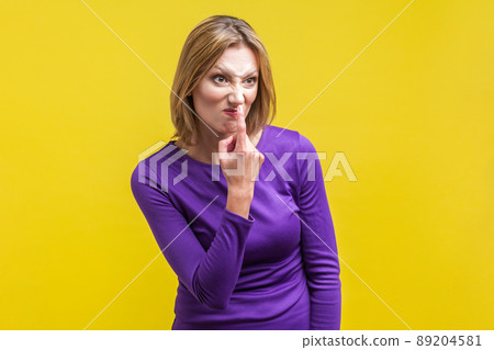 Portrait of angry young woman in tight purple dress looking aside and pointing at her nose, saying to trickster you are liar, body language. indoor studio shot isolated on yellow background 89204581