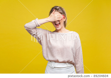 Portrait of confused, shocked or scared woman with fair hair in blouse standing, covering her eyes, don't want to watch. fear or shame expression. indoor studio shot isolated on yellow background Portrait of confused, shocked or scared woman with fair hair in blouse standing, covering her eyes, don't want to watch. fear or shame expression. indoor studio shot isolated on yellow background 89204604