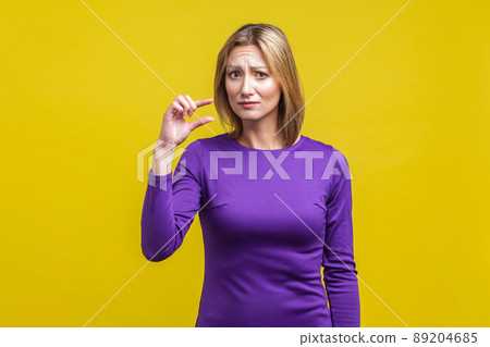 Portrait of disappointed woman in elegant purple dress frowning and showing a little bit gesture, asking some more, dissatisfied upset with amount. indoor studio shot isolated on yellow background Portrait of disappointed woman in elegant purple dress frowning and showing a little bit gesture, asking some more, dissatisfied upset with amount. indoor studio shot isolated on yellow background 89204685