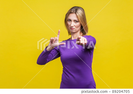 Portrait of bossy serious businesswoman in elegant purple dress showing loser gesture and pointing at camera, accusing for failure. indoor studio shot isolated on yellow background Portrait of bossy serious businesswoman in elegant purple dress showing loser gesture and pointing at camera, accusing for failure. indoor studio shot isolated on yellow background 89204705