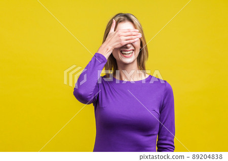 Portrait of bashful positive woman in elegant purple dress covering eyes with hand and laughing, shy to look. indoor studio shot isolated on yellow background Portrait of bashful positive woman in elegant purple dress covering eyes with hand and laughing, shy to look. indoor studio shot isolated on yellow background 89204838