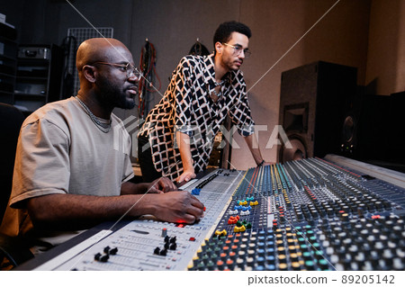 Modern mature Black sound engineer and stylish young singer working on music track in recording studio 89205142