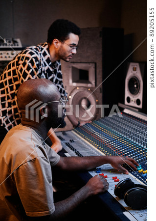 Vertical shot of modern mature African American producer and young singer creating music track in recording studio 89205155
