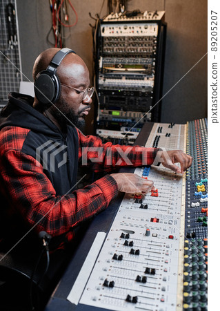 Vertical shot of modern African American male audio engineer using mixing console to create music 89205207