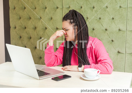 Portrait of unhappy confused young woman with black dreadlocks hairstyle in pink blouse sitting looking at screen, pinching nose with and pleased to stop showing bold video through web camera. indoor 89205266