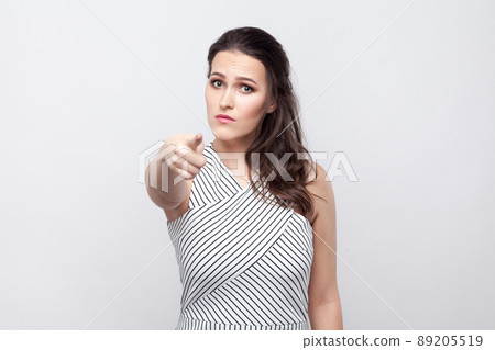 You. Portrait of serious beautiful young brunette woman with makeup and striped dress standing, looking and pointing at camera. indoor studio shot, isolated on grey background. You. Portrait of serious beautiful young brunette woman with makeup and striped dress standing, looking and pointing at camera. indoor studio shot, isolated on grey background. 89205519
