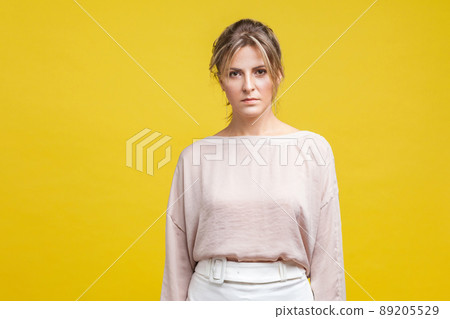 Portrait of unhappy young woman with messy blonde hair in casual blouse standing, looking dissatisfed and tired, worried about problems difficulties, indoor studio shot isolated on yellow background 89205529