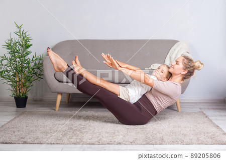 Young attractive mother and charming daughter practicing yoga at home, standing in boat pose, happy family doing gymnastics exercise together, fitness training with child. workouts with kid indoor 89205806