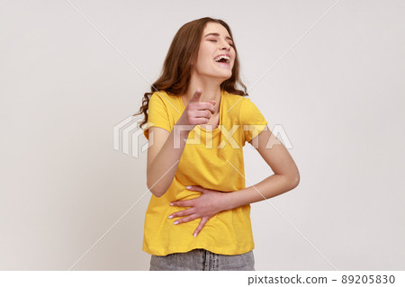 Hey, you are ridiculous. Teenager girl in yellow T-shirt laughing, holding stomach and pointing to camera, taunting you, can't stop hysterical laughter. Indoor studio shot isolated on gray background. Hey, you are ridiculous. Teenager girl in yellow T-shirt laughing, holding stomach and pointing to camera, taunting you, can't stop hysterical laughter. Indoor studio shot isolated on gray background. 89205830