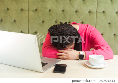 overwork and sleeping. Portrait of tired kind beautiful young freelancer with black dreadlocks in pink blouse is sitting in cafe and fall asleep on the table after too long working. Indoor overwork and sleeping. Portrait of tired kind beautiful young freelancer with black dreadlocks in pink blouse is sitting in cafe and fall asleep on the table after too long working. Indoor 89205833