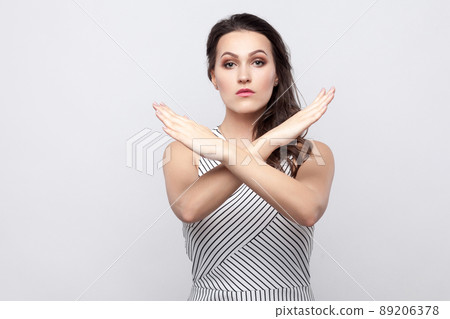 There is no way. Portrait of serious beautiful young brunette woman with makeup and striped dress standing with crossed hands and warning wrong way. indoor studio shot, isolated on grey background. There is no way. Portrait of serious beautiful young brunette woman with makeup and striped dress standing with crossed hands and warning wrong way. indoor studio shot, isolated on grey background. 89206378