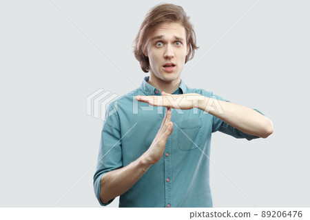 I need more time. Portrait of worry handsome long haired blonde young man in blue casual shirt standing with time out sign and looking at camera. indoor studio shot, isolated on light grey background. I need more time. Portrait of worry handsome long haired blonde young man in blue casual shirt standing with time out sign and looking at camera. indoor studio shot, isolated on light grey background. 89206476