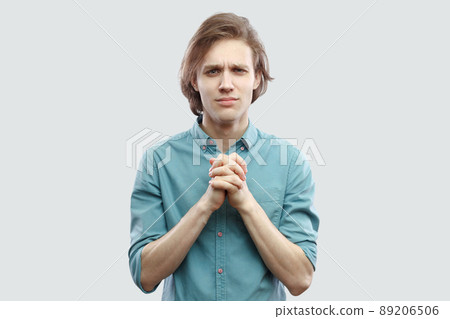 Please help me. Portrait of hopeful handsome long haired blonde young man in blue shirt standing with palm hand and hope for help or forgiveness. indoor studio shot, isolated on light grey background. Please help me. Portrait of hopeful handsome long haired blonde young man in blue shirt standing with palm hand and hope for help or forgiveness. indoor studio shot, isolated on light grey background. 89206506