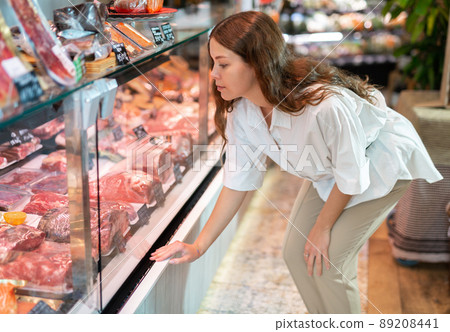 Young girl examines the production in the department of the butcher shop in the supermarket Young girl examines the production in the department of the butcher shop in the supermarket 89208441