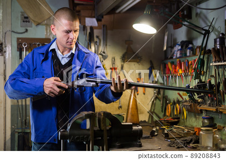 Double-barreled hunting rifle in hands of gunsmith in weapons workshop Double-barreled hunting rifle in hands of gunsmith in weapons workshop 89208843