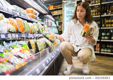 Focused girl in a supermarket chooses frozen vegetables on a substrate Focused girl in a supermarket chooses frozen vegetables on a substrate 89208861